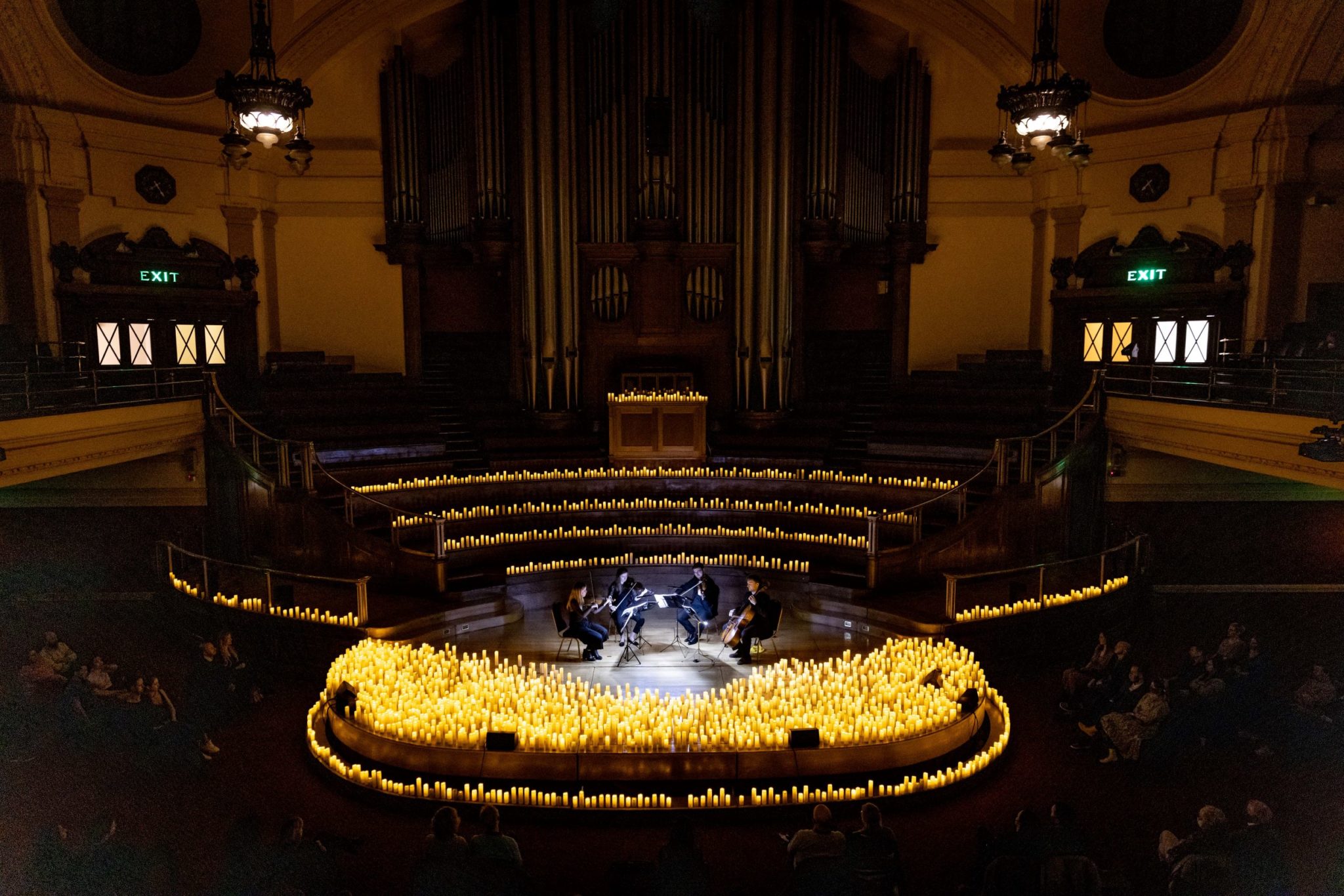 A wide shot of a stage covered in candles and a string quartet performing.